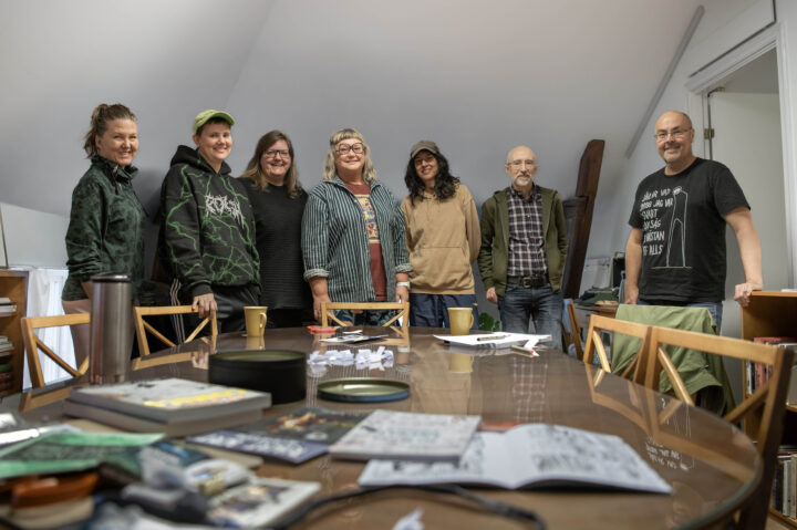 Sex glada deltagare poserar, inomhus framför ett bord med fanzine. Verksamhetsledaren Victor Estby står bredvid.